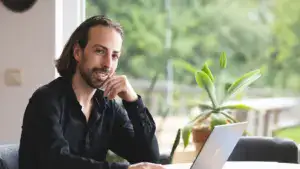 תמונה של גבר יושב במשרד עם מחשב נייד, רקע של נוף ירוק מחוץ לחלון, מייצג עיצוב פנים ופתרונות אדריכליי.